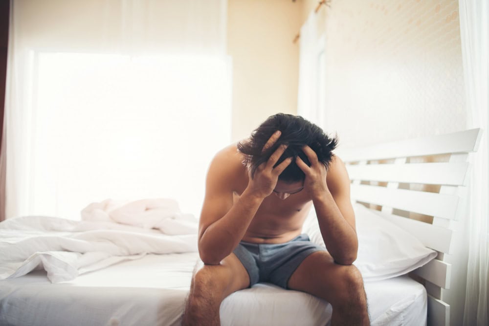 Dizzy man holding head in bedroom, health concern, wellness, medical issue.