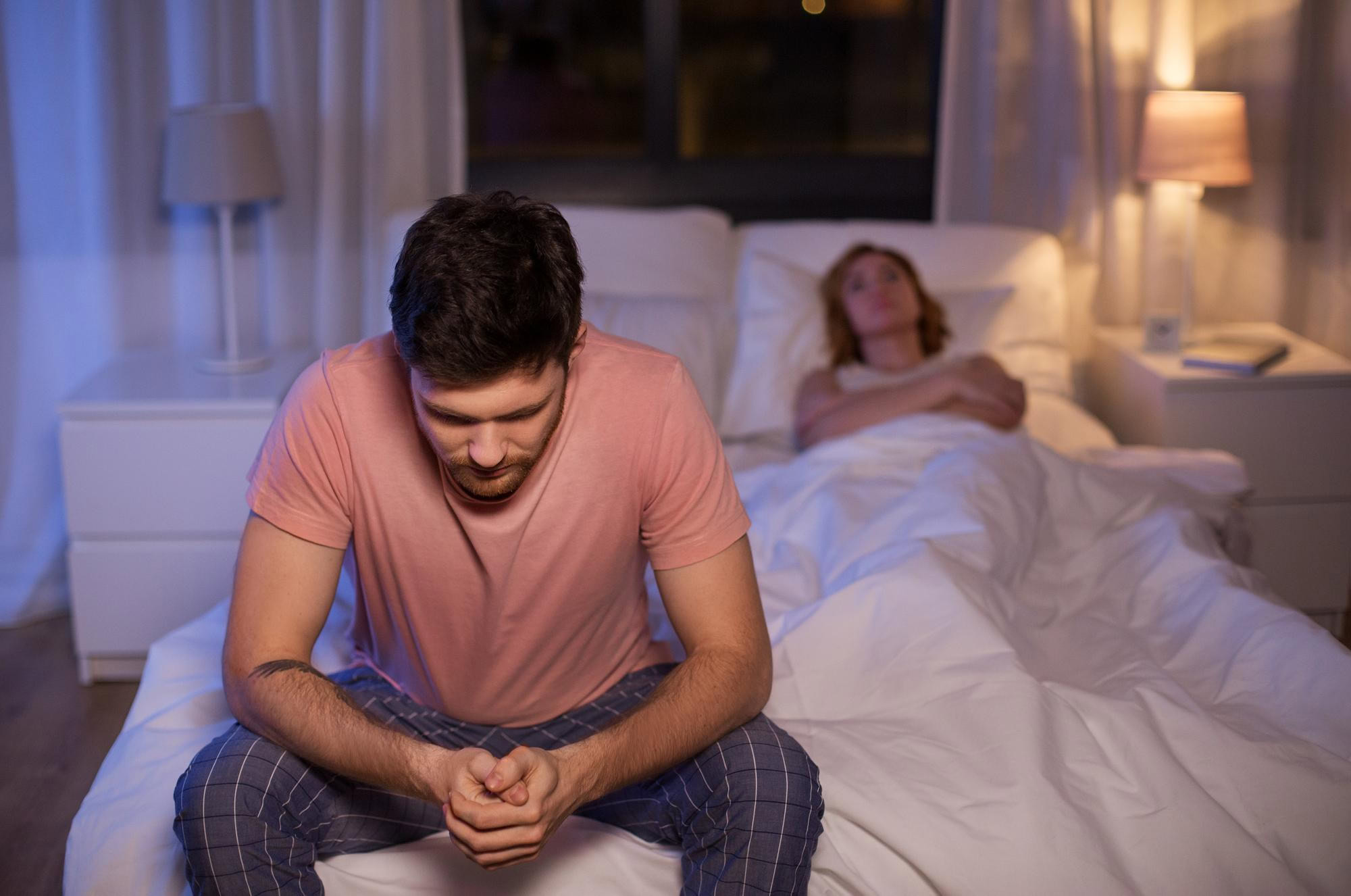 Sad man with wife suffering from illness, feeling worried at night in bedroom.