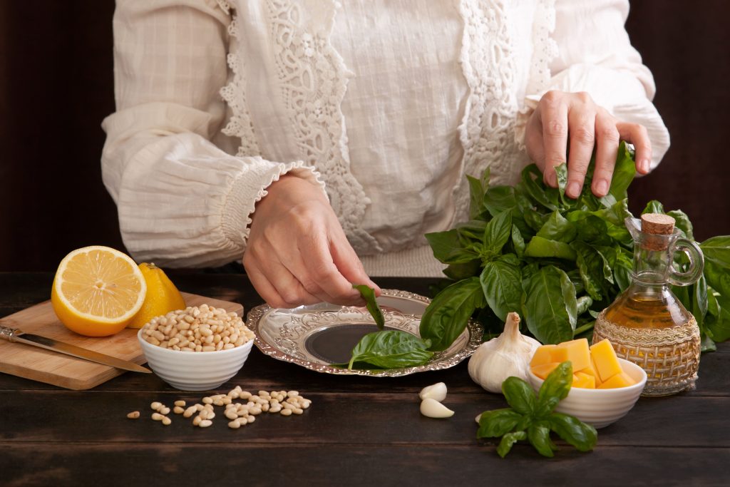 Herbal medicine preparation with basil, garlic, lemon, and oils on a wooden table.