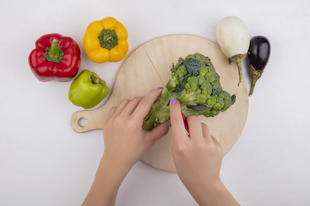 Fresh broccoli and colorful bell peppers on a cutting board for healthy cooking.